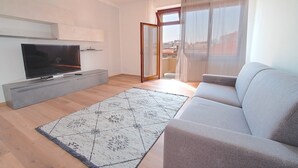 A modern living room with a flat-screen TV, grey sofa, and a patterned rug.