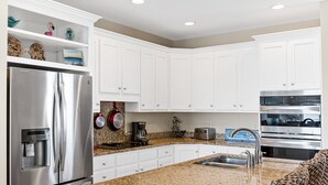 Una cocina moderna con gabinetes blancos, electrodomésticos de acero inoxidable, encimeras de granito y horno integrado.