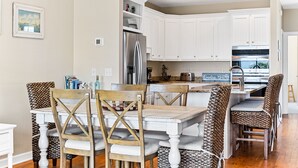 Una cocina moderna con armarios blancos, un refrigerador de acero inoxidable y un horno empotrado. Hay una zona de comedor con una mesa de madera y sillas estampadas.