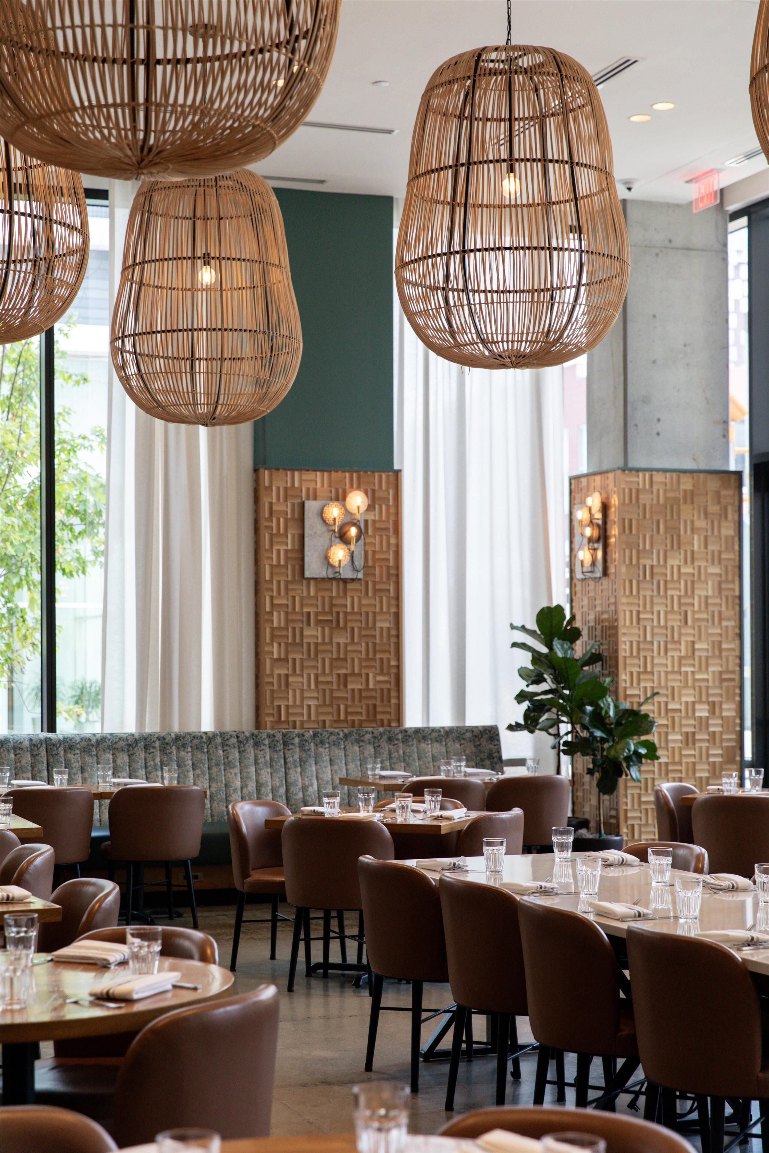 A restaurant with round tables, brown chairs, and woven pendant lights.