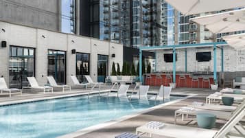 A rooftop pool area with lounge chairs, a bar, and a view of a modern building.