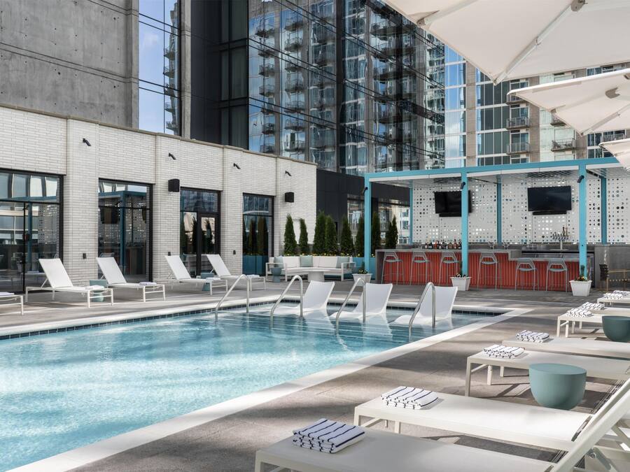 A rooftop pool area with lounge chairs, a bar, and a view of a modern building.