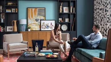 A modern living room with a sofa, armchairs, a coffee table with books and snacks, and a bookshelf with various items.