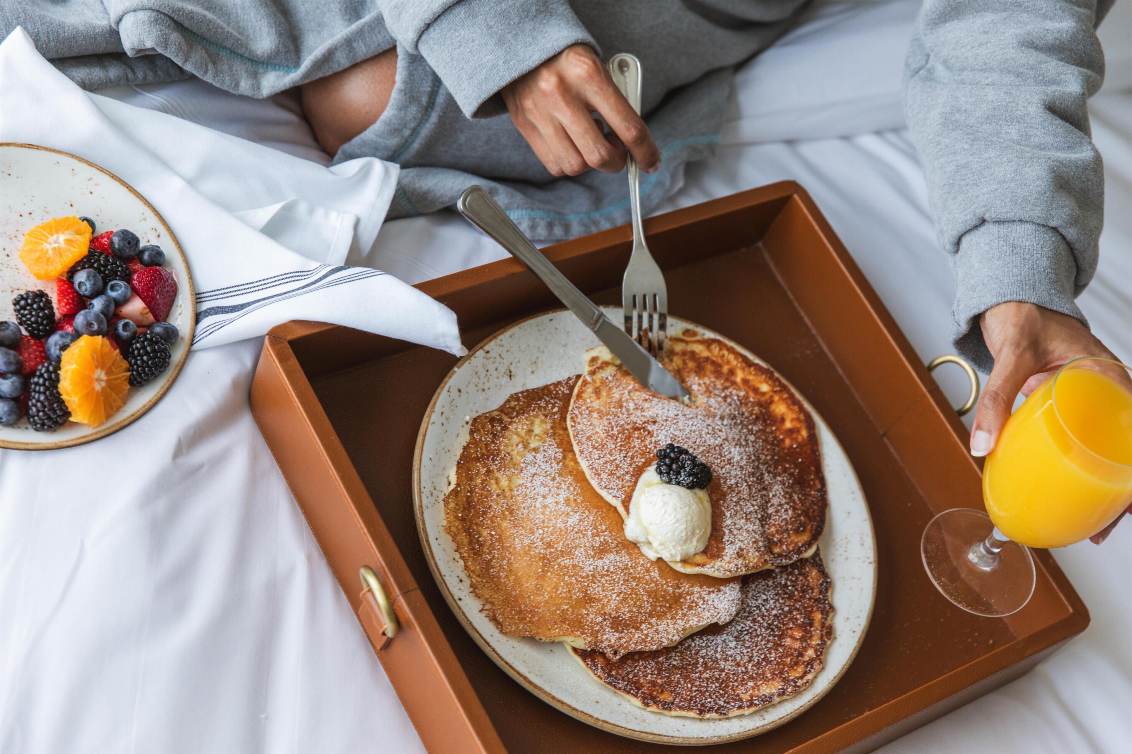 Een ontbijfwagen met pannenkoeken, bessen en een glas sinaasappelsap op een bed.