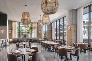 Un vaste espace dédié à la salle à manger, avec de nombreuses tables et chaises, de grandes fenêtres et des luminaires suspendus en osier.