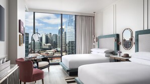 Habitación de hotel con dos camas, un escritorio, una silla y un ventanal con vistas a la ciudad.