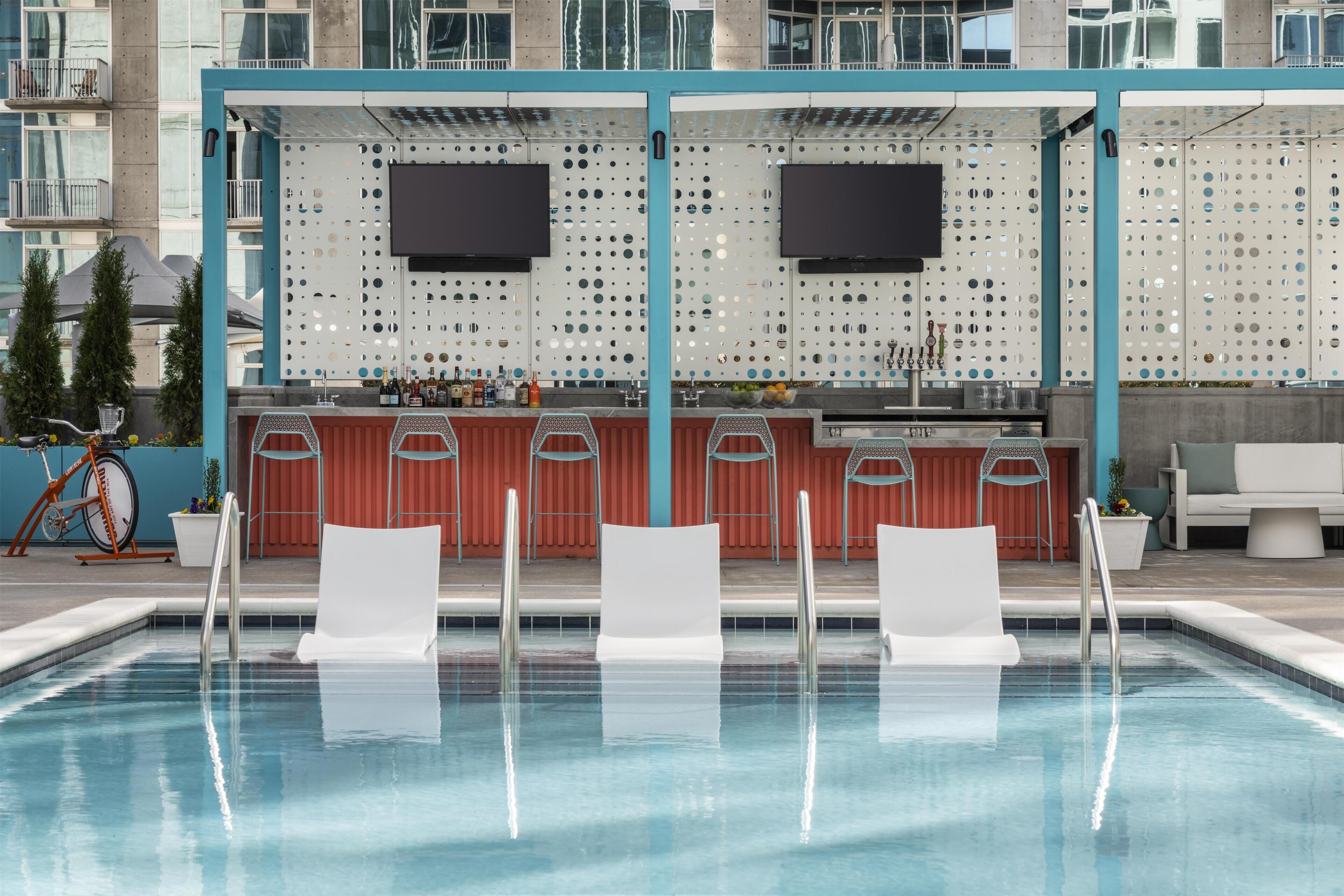 A swimming pool with lounge chairs, a bar area with bottles, and a wall with circular cutouts.