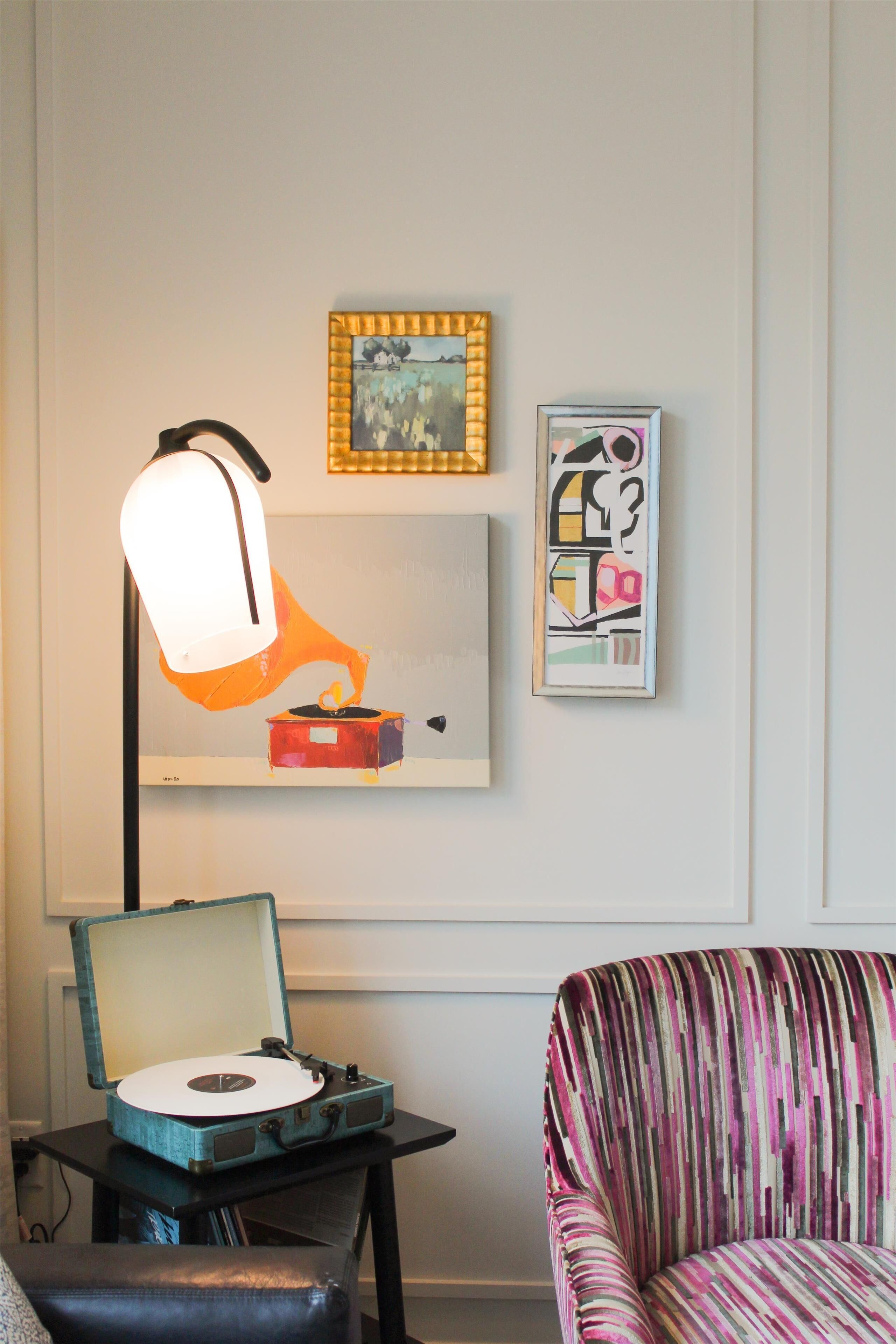 Une pièce avec une platine vinyle posée sur une table, une chaise et des œuvres d’art accrochées au mur.