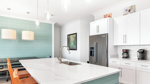 A modern kitchen with a central island, white cabinetry, and a teal accent wall. - 😎 Night Heron, East. ⭐️⭐️⭐️⭐️⭐️ 6BR. Heated Pool. Beachview. Gorgeous! (Gulf Shores)