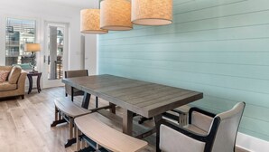 A dining area with a wooden table and benches, a light blue wall, and three wicker lamps. - 😎 Night Heron, East. ⭐️⭐️⭐️⭐️⭐️ 6BR. Heated Pool. Beachview. Gorgeous! (Gulf Shores)