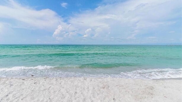 Een strand met helder turquoise water en een zandkust, onder een lichtbewolkte lucht.