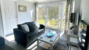 A modern living room with a black sofa, a coffee table, and a TV on a stand. - 2 Bed Villa Sleeps 4 - Wifi, Garden, Sea Views (Looe)