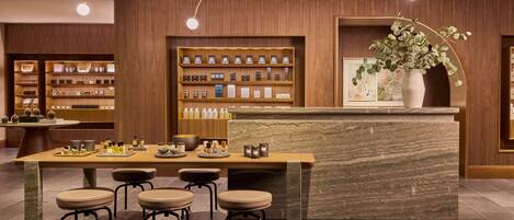 A modern bar area with a marble counter, wooden shelves with bottles, and a potted plant.
