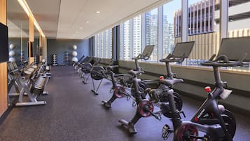 Une salle de sport équipée de vélos d’appartement, de miroirs et offrant une vue sur de hauts immeubles.