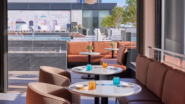 A modern rooftop lounge with seating and tables, a cityscape view, and a decorative wall mural. - Omni Boston Hotel at the Seaport (Boston)