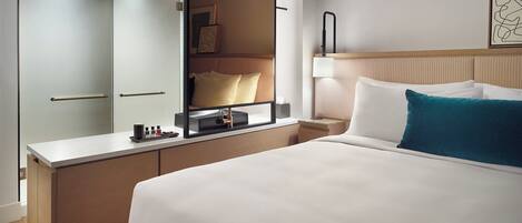 A hotel room with a bed, a bedside table, a nightstand, a mirror, a wardrobe, and a wall-mounted artwork.