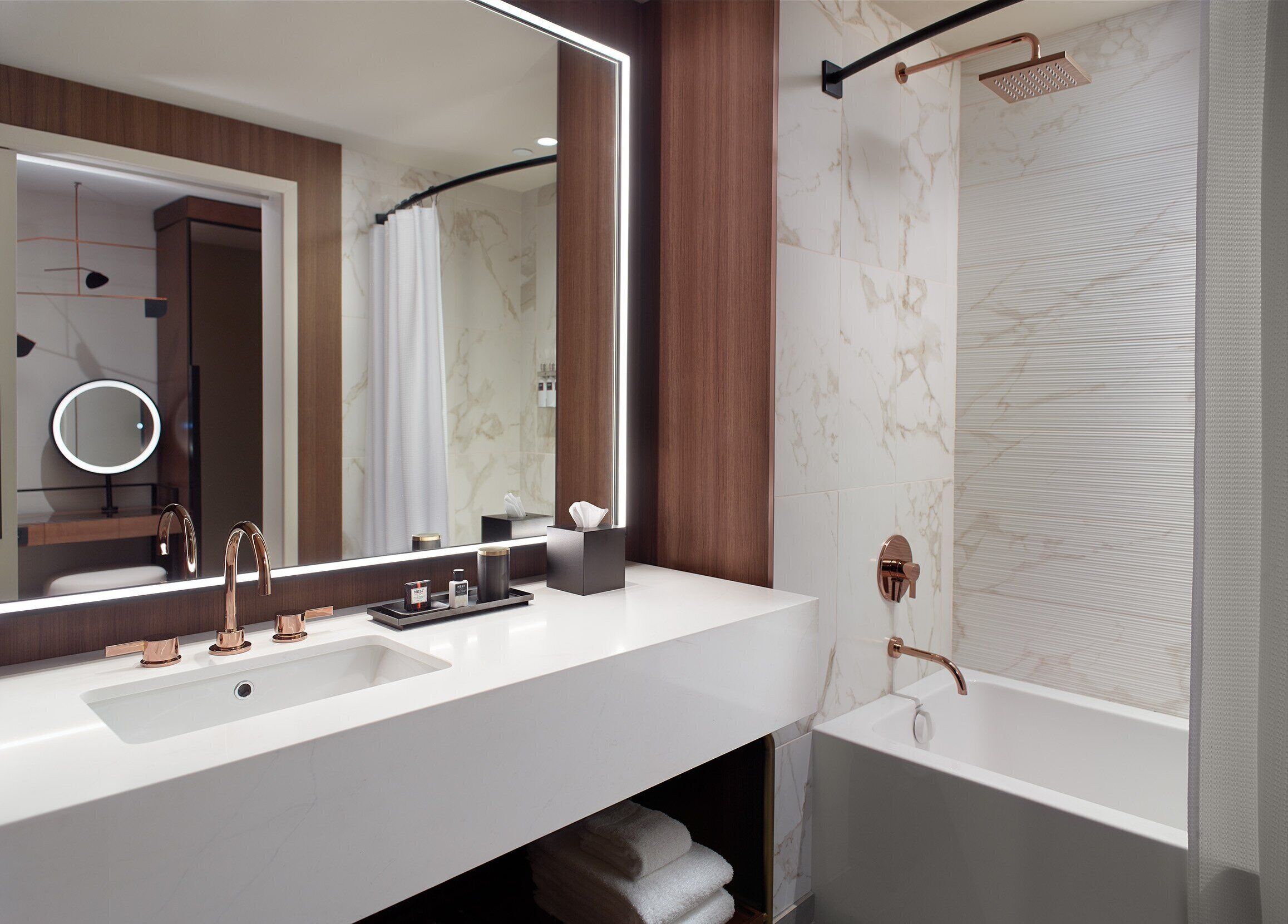 A modern bathroom with a white sink, two faucets, a large mirror, and a shower area.