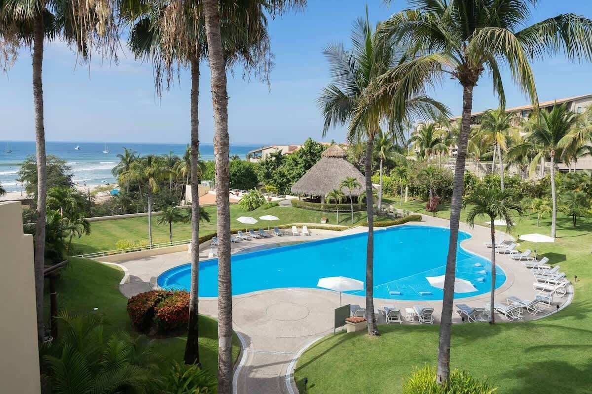Um resort com uma piscina grande cercada por palmeiras e vista para o oceano.