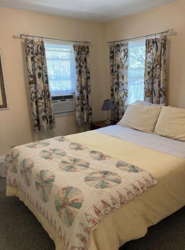 A bedroom with a bed, floral curtains, a window, and a lamp.