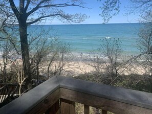 A wooden deck overlooking a beach with clear blue water and distant land.