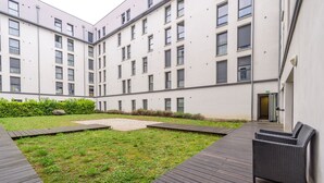 A courtyard with a grassy area, a wooden deck, and a building with multiple windows and a door. - Auriol - Appt contemporain (Toulouse)