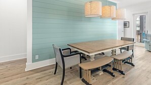 A dining area with a wooden table and chairs, a teal accent wall, and hanging wicker lamps. - 😎 Night Heron, West. ⭐️⭐️⭐️⭐️⭐️ 6BR. Heated Pool. Beachview. Gorgeous! (Gulf Shores)