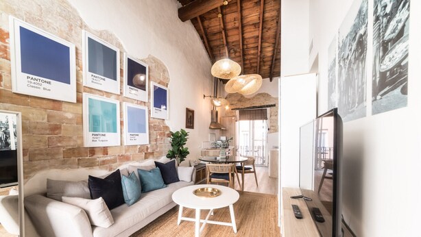 Una sala de estar con una pared de ladrillo, un sofá blanco, una mesa de centro redonda y un televisor.