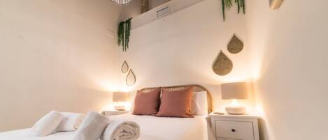 A neatly made bed with rolled towels, two bedside tables with lamps, and decorative wall hangings.
