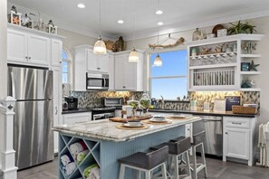A modern kitchen with white cabinetry, stainless steel appliances, and a central island with bar stools. - Beachfront Sleeps 14 | Hot Tub | Fire Pit and Deck (Galveston)