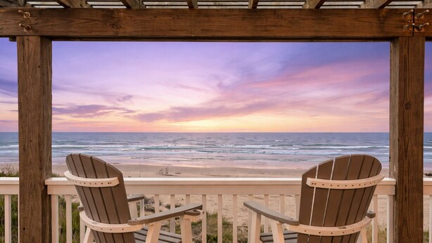 Un pontile di legno con due poltrone Adirondack rivolte verso una spiaggia al tramonto.