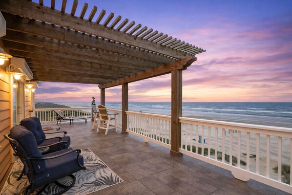 A covered outdoor seating area with a view of the ocean, featuring a pergola, chairs, and a railing. - Beachfront Sleeps 14 | Hot Tub | Fire Pit and Deck (Galveston)
