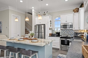 A modern kitchen with white cabinets, stainless steel appliances, and a central island with bar stools. - Beachfront Sleeps 14 | Hot Tub | Fire Pit and Deck (Galveston)