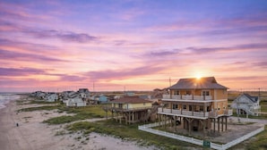 Una proprietà fronte mare con diverse case su palafitte, un molo che si protende nell'acqua e un tramonto sullo sfondo.