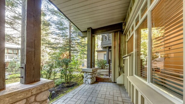 A covered porch with stone columns, a stone bench, and a view of a forested area.