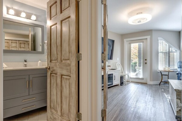 Un baño moderno con un espejo grande, tocador y puerta de madera.