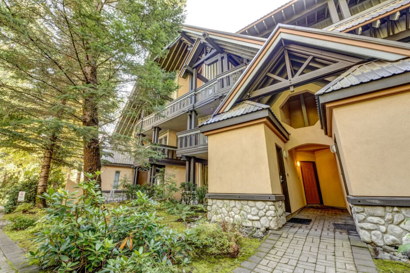 A multi-story building with a stone foundation, balconies, and a pathway leading to the entrance.