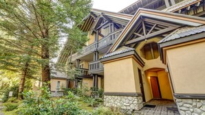A multi-story building with a stone foundation, balconies, and a pathway leading to the entrance.