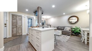 A modern kitchen with white cabinetry, a central island, and a dining area with a gray sofa and a round mirror on the wall.