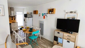 Un espace de vie compact comprenant un coin repas, une kitchenette et un téléviseur posé sur un meuble en bois.