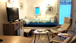 Un salon confortable avec un canapé, deux fauteuils, une table basse, un téléviseur et un escalier.