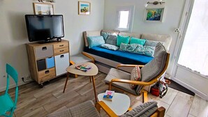 Un salon comprenant un canapé, un téléviseur, un meuble en bois et une table sur laquelle se trouve un livre.
