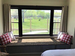 A room with a large window, a radiator, a bench with checkered cushions, and a bed. - Swisher Farmhouse at Granny Flats (Spearfish)