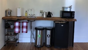 Una cocina compacta con encimera de madera, un lavamanos, un microondas, una tetera y dos cubos de basura.