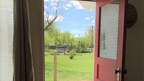 Una habitación con piso de madera, una puerta roja y vista a un patio cubierto de césped.