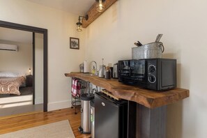 Une cuisine compacte équipée d’un four à micro-ondes, d’un grille-pain et d’une bouilloire encastrés, d’une petite poubelle et d’un plan de travail en bois.