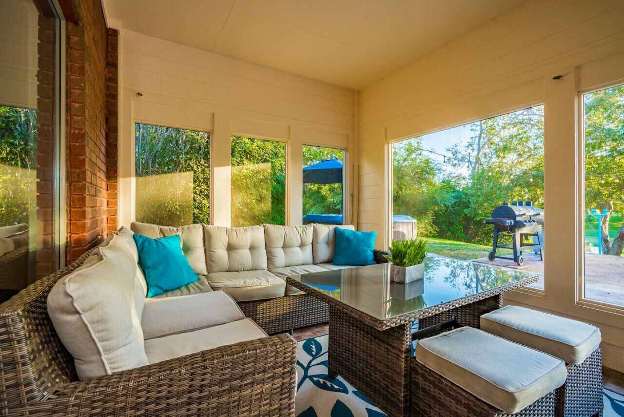 A sunroom with a large sectional sofa, a glass coffee table, and wicker furniture.