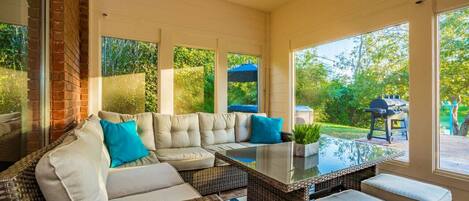 A sunroom with a large sectional sofa, a glass coffee table, and wicker furniture.