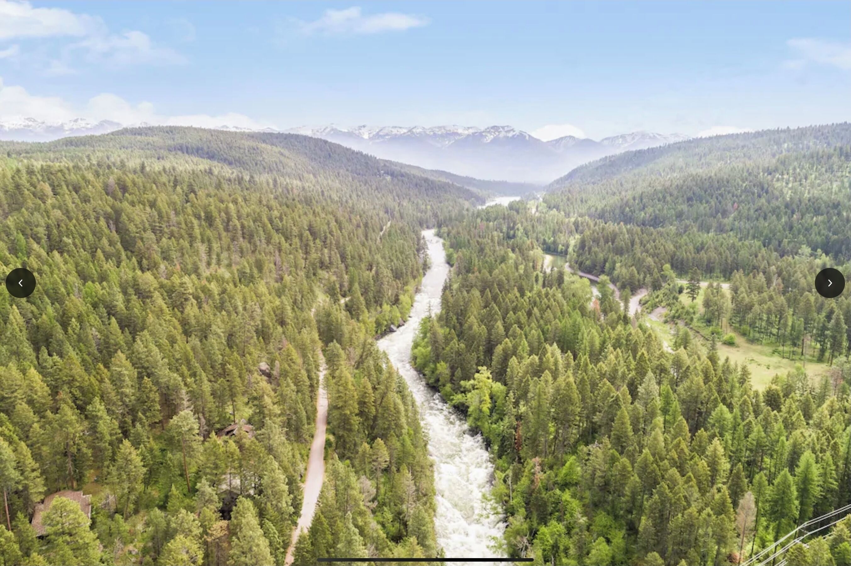 Ein Fluss schlängelt sich durch einen dichten Wald, im Hintergrund erheben sich Berge.