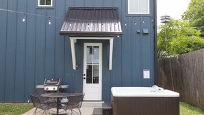 A blue building with a front door, a hot tub, and a grill outside. - Lux 3BR Cottage | Walk to Rose District | Sleeps 6 (Broken Arrow)