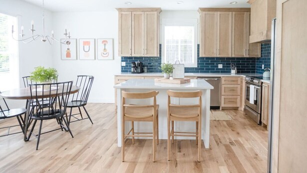 Een moderne keuken met houten kastjes, een centraal eiland en een eethoek met stoelen.